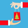 Santa Claus hand giving taking shopping paper bag with fir tree. Royalty Free Stock Photo