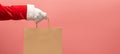 Santa Claus hand holding brown shopping paper bag on pink isolated background Royalty Free Stock Photo