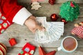 Santa Claus hand holding cash money against Christmas background, suggesting high expenses during the holidays