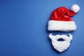 Santa Claus hat and beard on blue background, flat lay