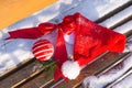 Santa Claus hat, red ball and red bow on a snow-covered bench. Christmas and New Year concept Royalty Free Stock Photo