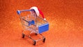 Santa Claus hat on a shopping trolley on a bright orange shiny background. The concept of Christmas shopping, New Year`s discount