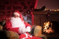 Santa Claus having a rest in a comfortable chair near the fireplace at home Royalty Free Stock Photo