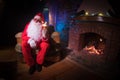 Santa Claus having a rest in a comfortable chair near the fireplace at home Royalty Free Stock Photo