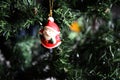 Santa Claus with his red cap, white beard and mustache, black belt, decorates the Christmas tree, hanging by a golden cord Royalty Free Stock Photo