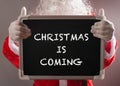 Santa Claus holding a black chalk board written with CHRISTMAS IS COMING Royalty Free Stock Photo