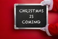 Santa Claus holding a black chalk board written with CHRISTMAS IS COMING on red Royalty Free Stock Photo