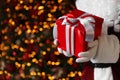 Santa Claus holding Christmas gift against blurred festive lights