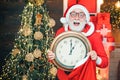 Santa Claus holding clock with countdown to Christmas or New Year Santa Claus in wooden home interior showing time on a Royalty Free Stock Photo