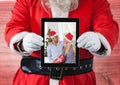 Santa claus holding a digital tablet with photo of christmas couple