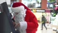 Santa Claus inserting credit card into bancomat entering a pin to receive money. Santa Claus withdrawing money from cash