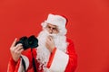 Santa Claus isolated on red background with a camera in his hands, looking with a pensive face. Christmas photographer Royalty Free Stock Photo
