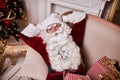 Santa Claus lay down to rest on the sofa with a bunch of gifts near the fireplace and christmas tree . New year and Merry Royalty Free Stock Photo