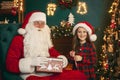 Santa Claus with a little cute girl open magical gift box in the room and get candy. Christmas time Royalty Free Stock Photo