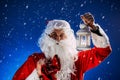 Santa Claus with a long white beard holds candle holder with burning candle against a snowing blue sky. Christmas Royalty Free Stock Photo