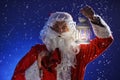 Santa Claus with a long white beard holds candle holder with burning candle against a snowing blue sky. Christmas Royalty Free Stock Photo