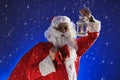 Santa Claus with a long white beard holds a lamp with a candle against a blue sky. It is snowing. Christmas Royalty Free Stock Photo