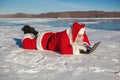 Santa Claus lying on the snow, looking at laptop n Royalty Free Stock Photo