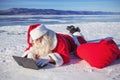 Santa Claus lying on the snow, looking at laptop n Royalty Free Stock Photo