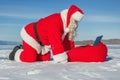 Santa Claus lying on the snow, looking at laptop news Royalty Free Stock Photo