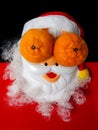 Santa claus mask with tangerines in place of the eyes. New year and Christmas concept. Funny Santa on black and red background,