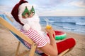 Santa Claus in party glasses with cocktail relaxing on beach. Christmas vacation