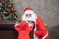 Santa Claus is playing peek a boo with little toddler baby in the house with fully decorated christmas tree for season celebration Royalty Free Stock Photo