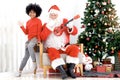 Santa Claus playing Ukulele with happy African American curry hair girl child singing Christmas songs front of decorative Royalty Free Stock Photo