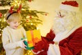 Santa Claus presented a gift for child near fir tree on Christmas Eve. Little boy opens the box and rejoices at the gift. Magic at Royalty Free Stock Photo