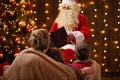 Santa Claus reading book for family. Mother and children sitting indoor near decorated xmas tree with lights - Merry Christmas and Royalty Free Stock Photo