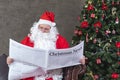 Santa Claus is reading Christmas news from the newspaper while sitting on the sofa couch by the christmas tree for long holiday Royalty Free Stock Photo