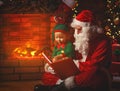 Santa claus reads a book to a little elf by Christmas tree Royalty Free Stock Photo