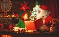 Santa claus reads book to little elf by Christmas tree Royalty Free Stock Photo