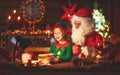 Santa claus reads letter to little elf by Christmas tree Royalty Free Stock Photo