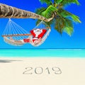 Santa Claus relax in hammock under palm tree at island tropical beach with handwritten caption 2019 happy new year Royalty Free Stock Photo