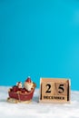 Santa Claus with scooter beside wooden block calendar set on the Christmas date 25 december on white wool and blue background. Cop