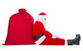 Santa Claus sit tired near big red Christmas sack full of presents isolated on white background Royalty Free Stock Photo