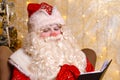 Santa claus sits in chair against background of christmas tree writes Royalty Free Stock Photo