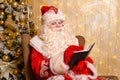 Santa claus sits in chair against background of christmas tree writes Royalty Free Stock Photo