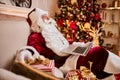 Santa Claus sitting at his home and reading email on laptop with ÃÂhristmas requesting or wish list near the fireplace and tree Royalty Free Stock Photo