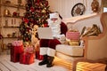 Santa Claus sitting at his home and reading email on laptop with ÃÂhristmas requesting or wish list near the fireplace and tree Royalty Free Stock Photo