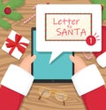 Santa claus is sitting at his workplace desk and receiving letter on his tablet