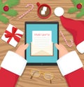 Santa claus is sitting at his workplace desk and receiving letter on his tablet