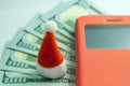 Santa Claus souvenir hat stands on the background of five hundred US dollars next to a mobile phone in a red case. The concept of