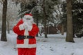 Santa Claus standing near a Christmas tree holding in a red bag gifts for children for Christmas around snow Royalty Free Stock Photo