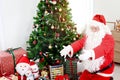 Santa Claus surrounded by gift boxes under Christmas tree, raising hands to give a hug to good children. Happy grandpa white beard Royalty Free Stock Photo