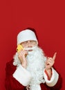 Santa Claus talking on the phone on a red background and looking away. Christmas greeting on the phone from Santa. Isolated. New Royalty Free Stock Photo