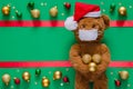 Santa claus teddy bear wearing mask and holding Christmas baubles on blurred green background with ornaments. Royalty Free Stock Photo