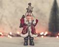 Santa Claus toy brings Christmas tree at blue snowy night bokeh background and blurred lights foreground. Royalty Free Stock Photo