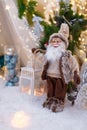 Santa Claus toy in brown clothes standing at white lantern. Fir tree branches and Christmas decorations on blurry background Royalty Free Stock Photo